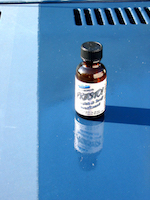 An old picture showing the reflection of an old bottle of PRESTO!™ on the hood of a car.